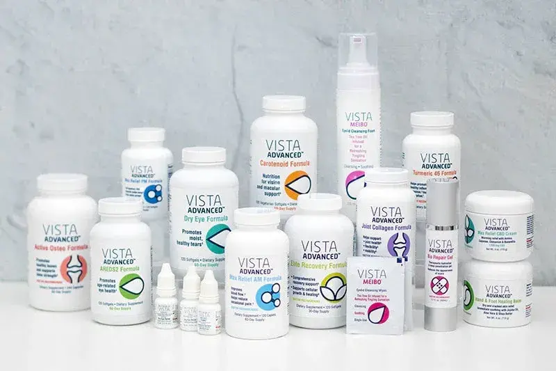 Various Vista Advanced health product bottles and jars are arranged on a white surface. Includes supplements, creams, and eyedrops, set against a gray background.